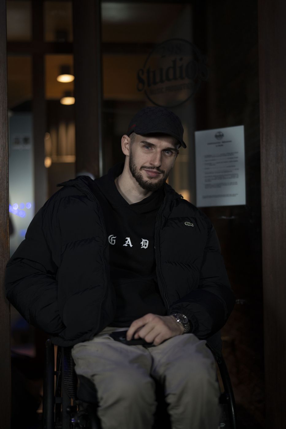 Valentin im Rollstuhl vor einem Musikstudio, in schwarzer Jacke und Cap